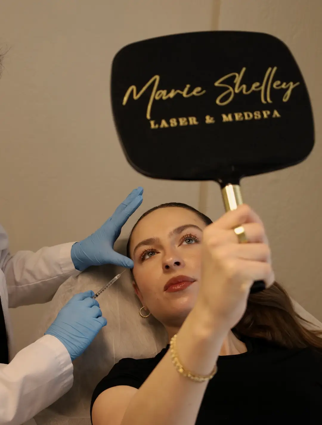 At the Roseville studio, a client holds up a Marie Shelley hand mirror while our nurse treats her forehead.